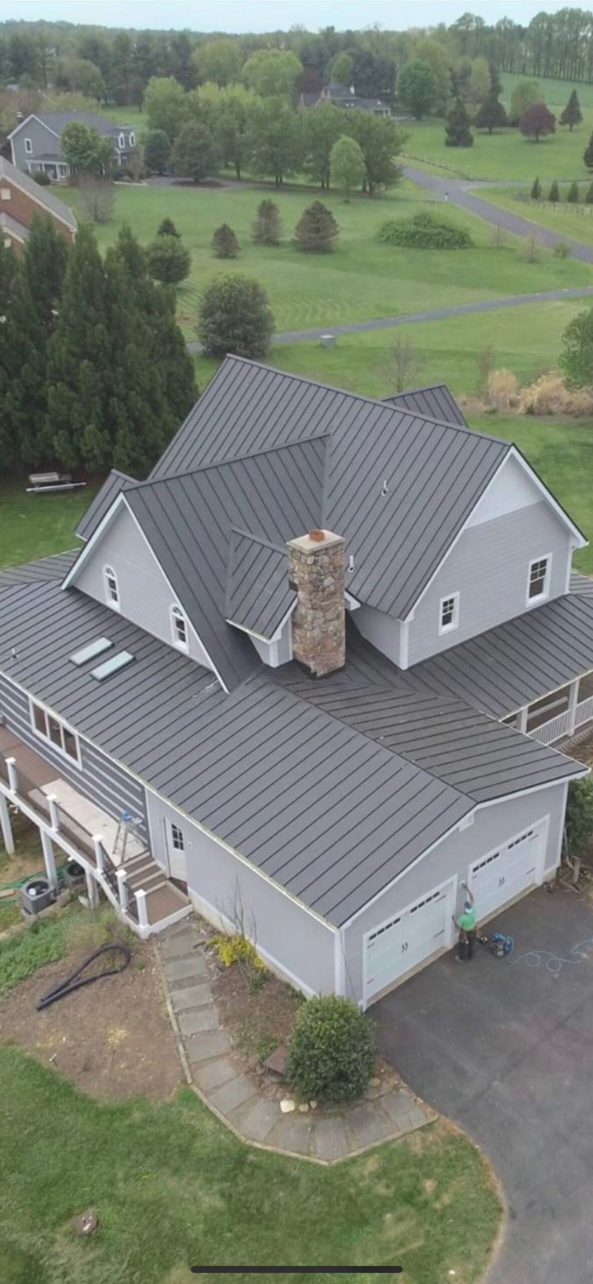 Aerial view of a Martinsburg WV home with a finished dark gray standing seam metal roof, stone chimney and two skylights