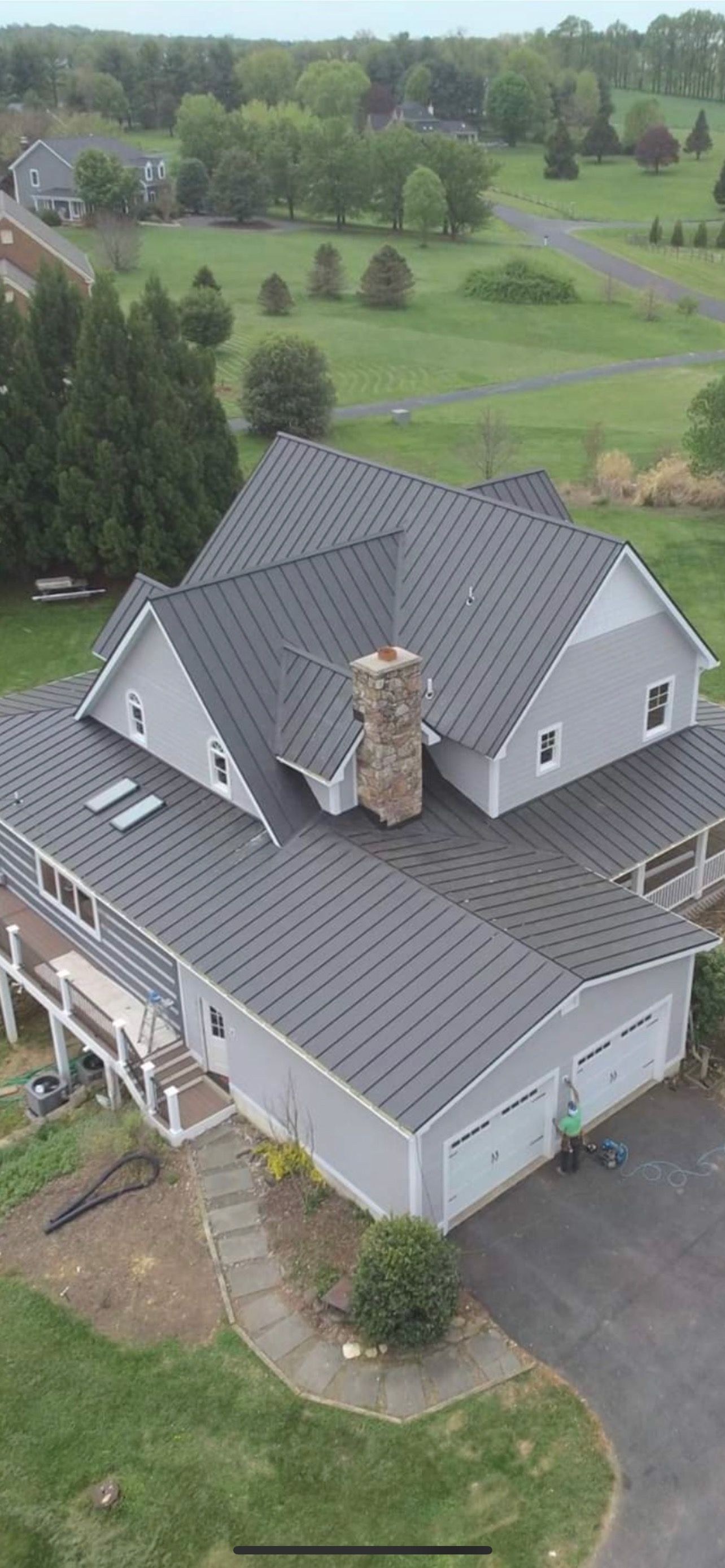 Aerial view of a Martinsburg WV home with a finished dark gray standing seam metal roof, stone chimney and two skylights