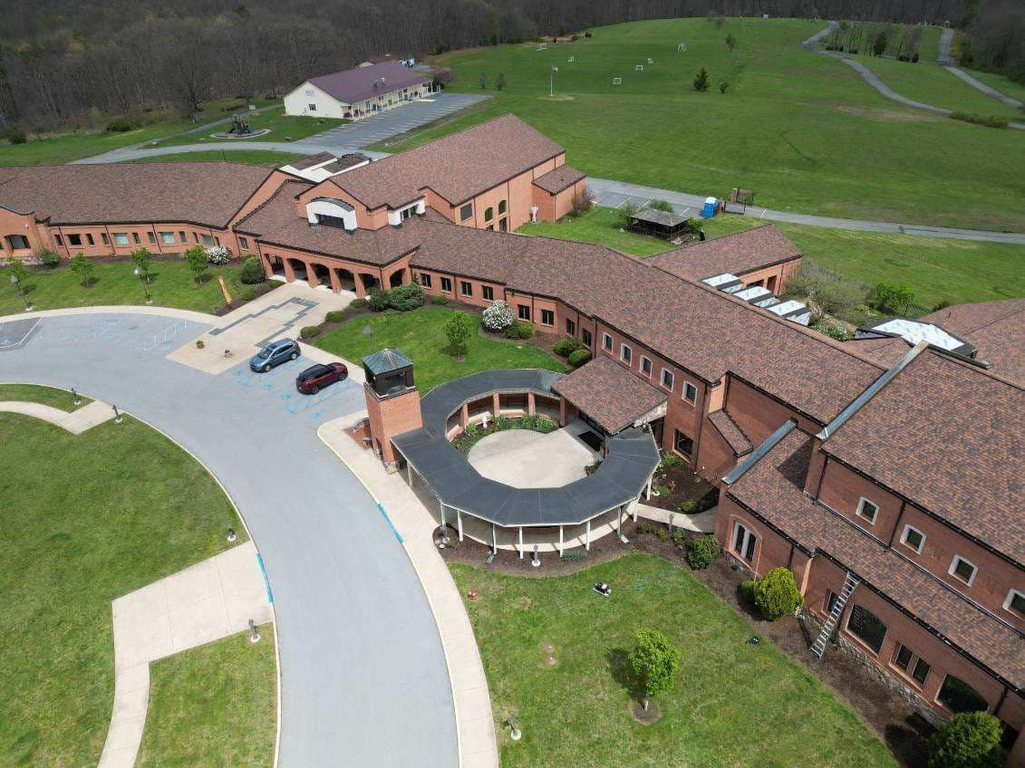 Aerial view of a large brick church campus with brown architectural asphalt shingle roofing and a ladder set for roof work, commercial shingle roofing by Black Stone Roofing in Martinsburg WV