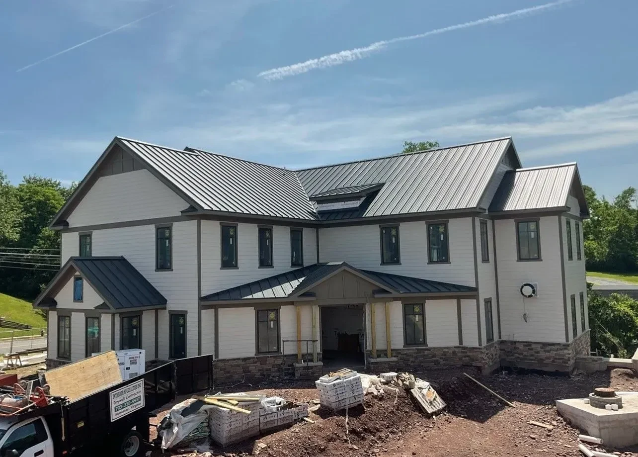 Dark charcoal standing seam metal roof installed on a large two story new construction building with white siding and stone veneer in the Martinsburg WV area