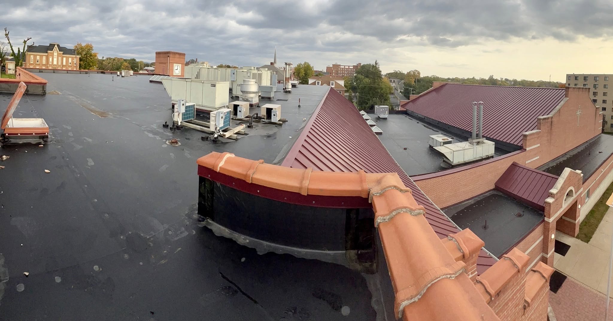 Maroon standing seam metal roof and black membrane flat roof on a brick church campus maintained by Black Stone Roofing