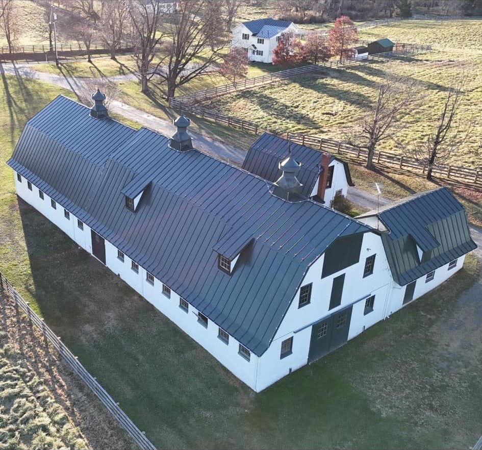 Aerial view of a long white barn with a dark standing seam metal roof and three cupolas on a farm property, metal roofing by Black Stone Roofing near Martinsburg WV