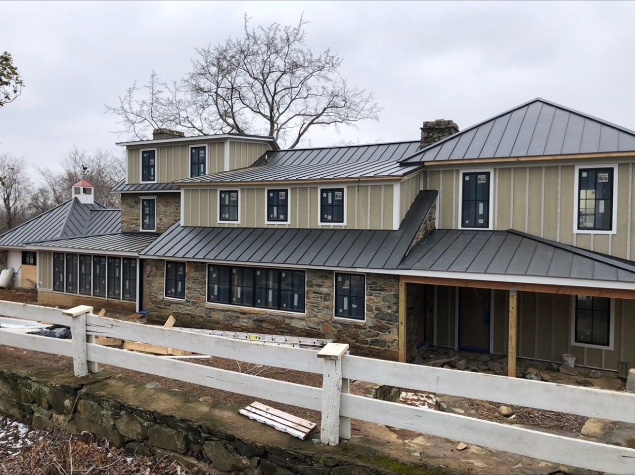 Large custom home near Martinsburg WV with a new charcoal standing seam metal roof above stone veneer and tan board and batten siding